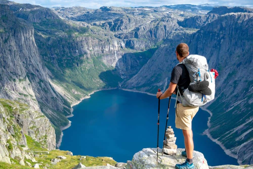 Ein Rucksacktourist steht auf einem Berggipfel in der Schweiz und blickt auf einen See.