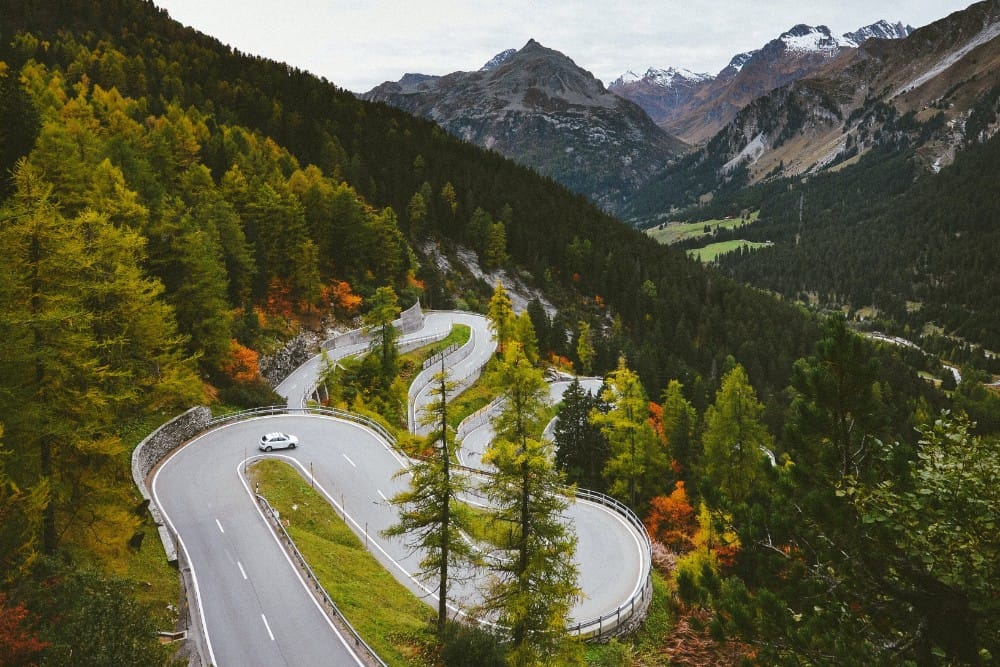 Ein Schweizer Auto fährt auf einem Roadtrip eine kurvenreiche Straße in den Bergen hinunter.