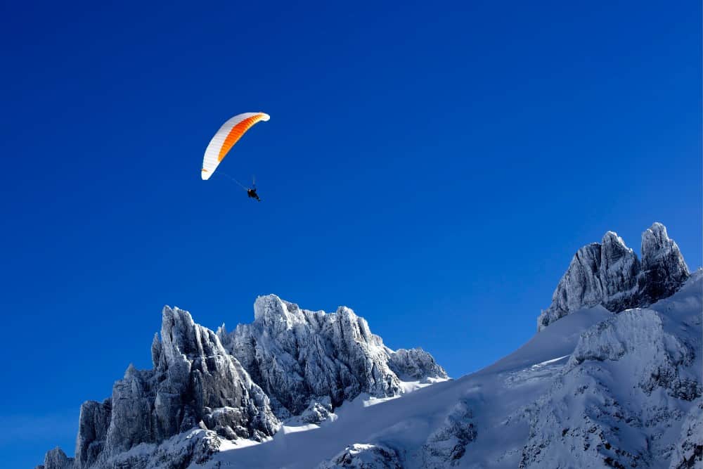 Eine Person fliegt mit dem Gleitschirm über den schneebedeckten Berg in Engelberg.
