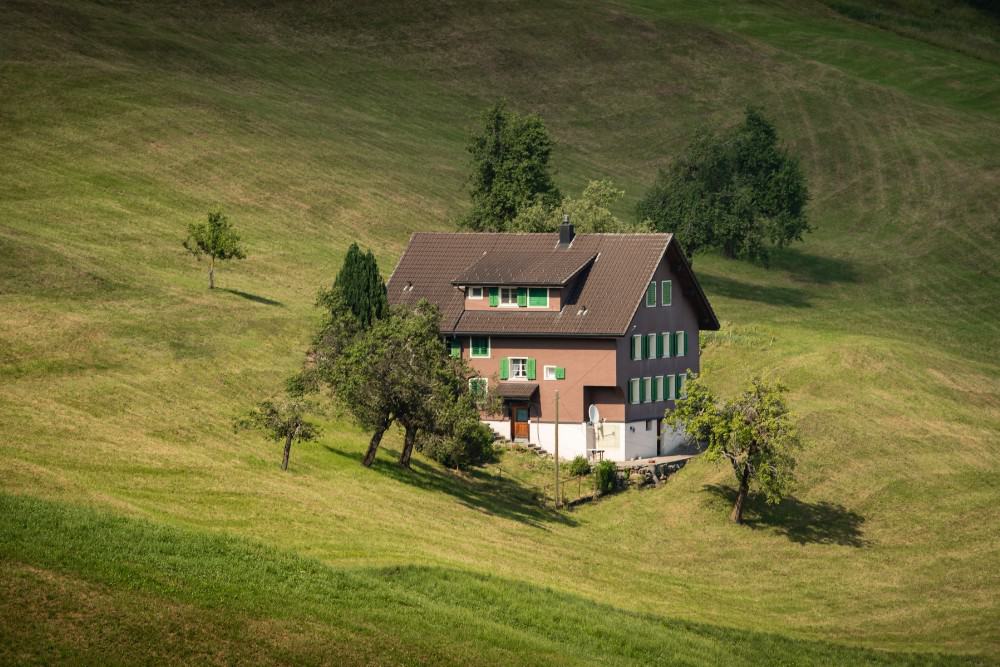Beschreibung: Ein braunes Ferienhaus liegt auf einem grünen Hügel in der Schweiz.