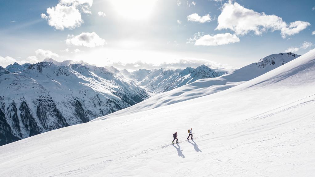 Zwei Personen fahren einen schneebedeckten Berg hinunter.